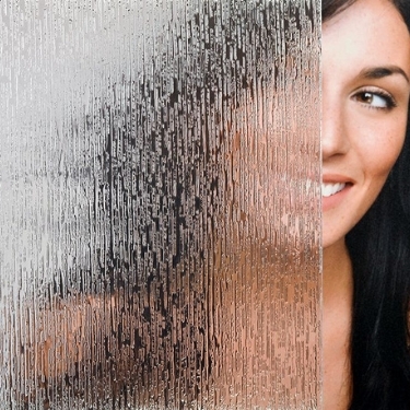 Woman standing behind rain pattern shower glass. 