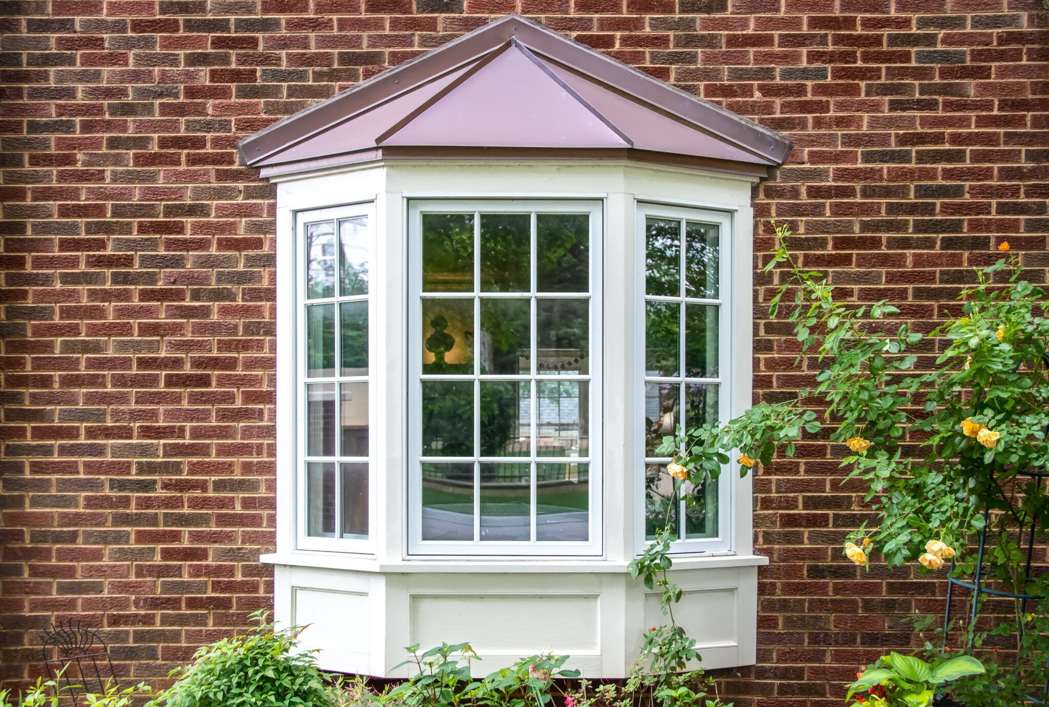 Bay window with copper roof on traditional brick home with flowe